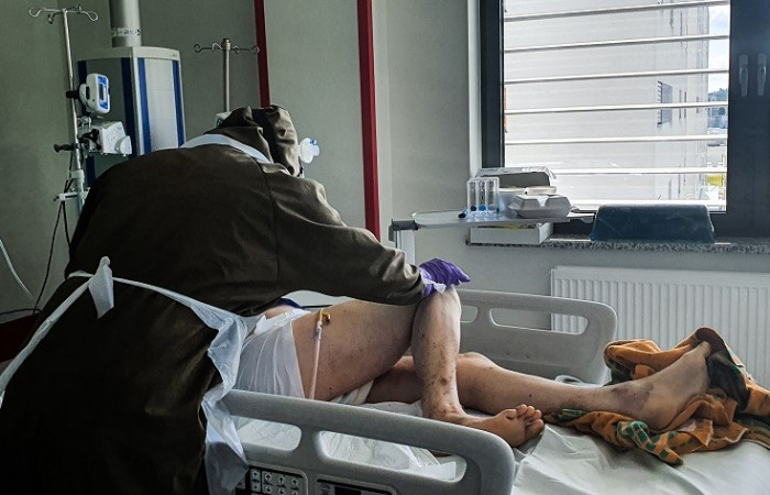 Oddział covid - pracownik w kombinezonie ochronnym pochyla się nad łóżkiem pacjenta 