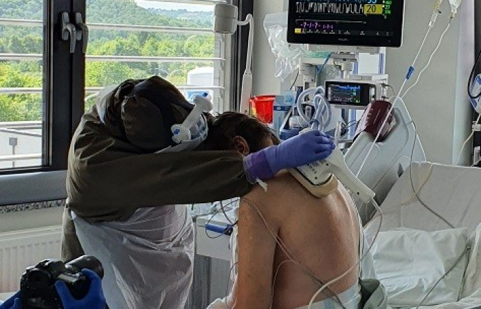 Oddział covid - pracownik w kombinezonie ochronnym pochyla się nad łóżkiem pacjenta 