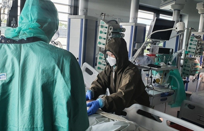 Oddział covid - pracownik w kombinezonie ochronnym pochyla się nad łóżkiem pacjenta 